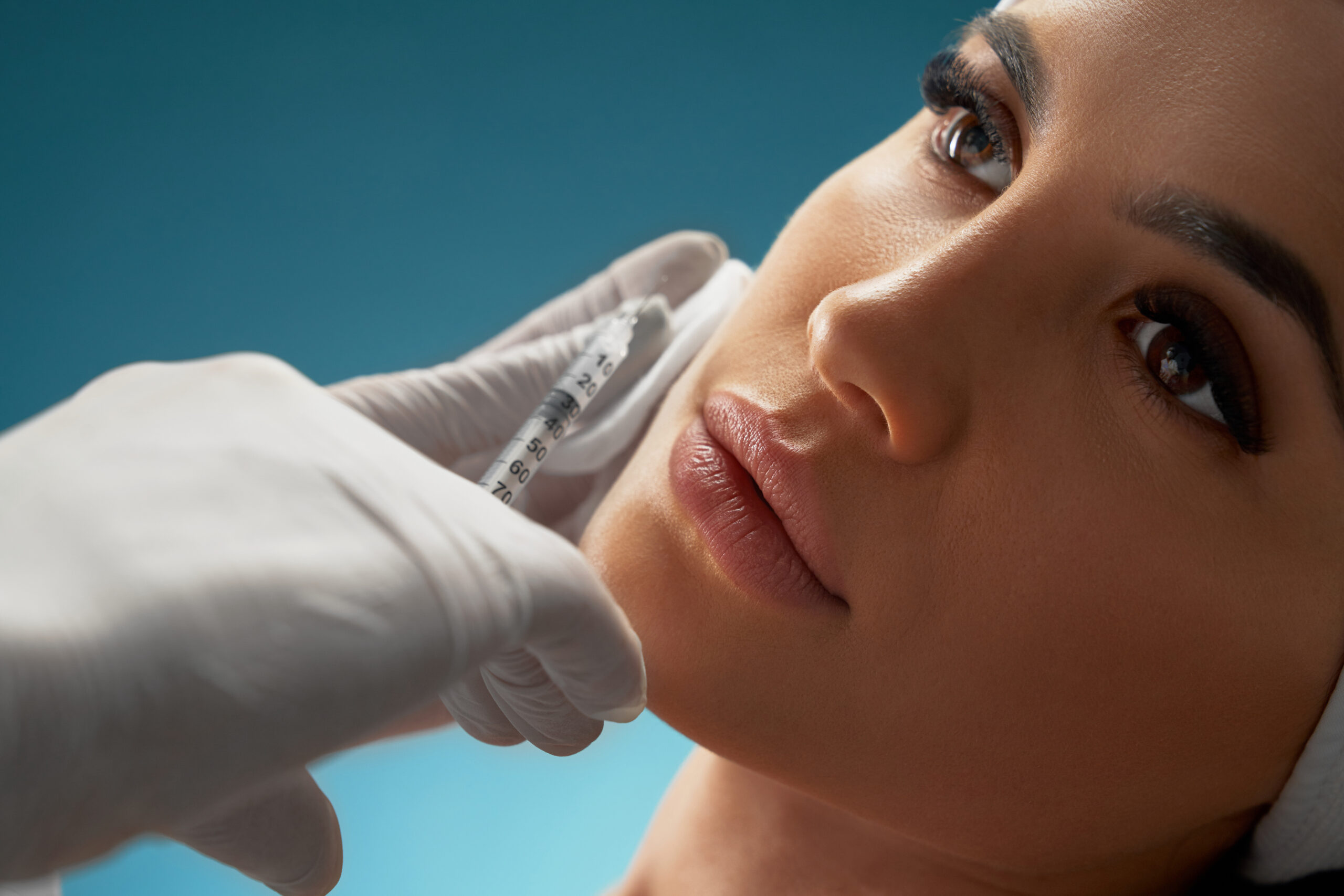 Cosmetologist using syringe to correct female face.