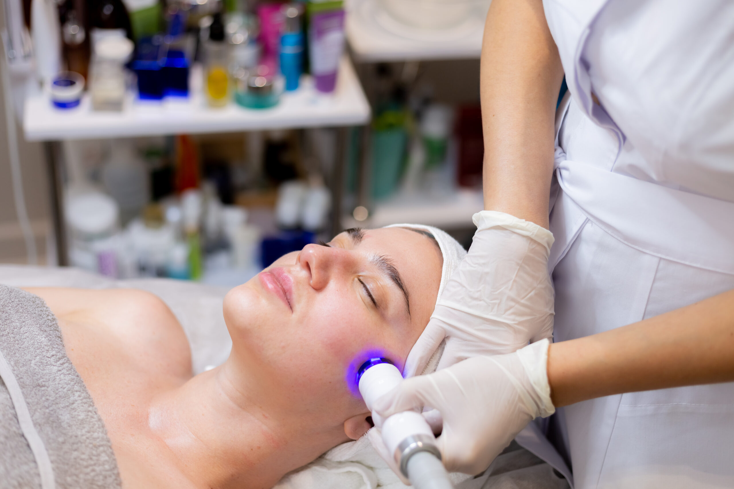 A young beautiful girl lies on the beautician's table and receives procedures with a professional apparatus for skin rejuvenation and moisturizing