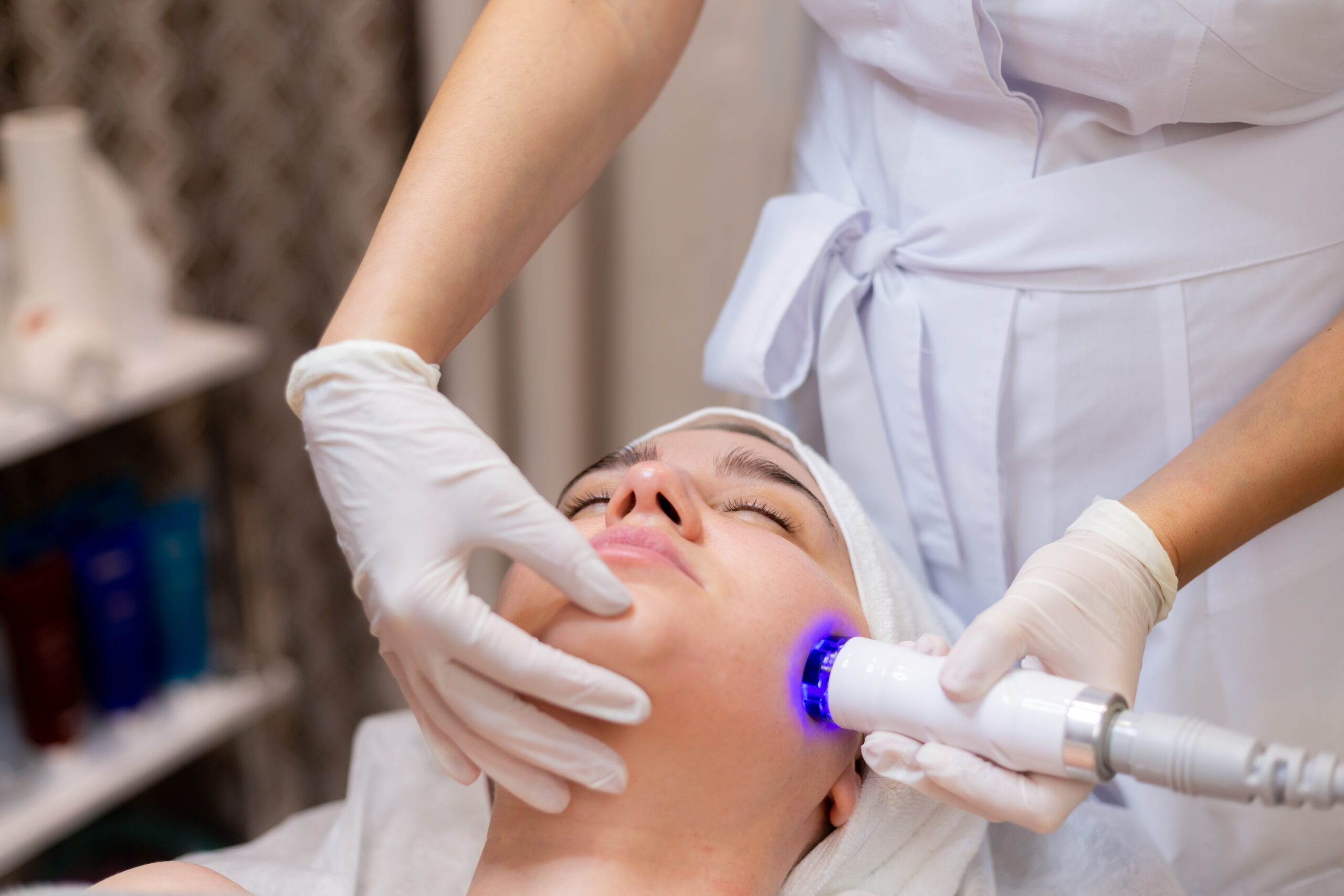 A young beautiful girl lies on the beautician's table and receives procedures with a professional apparatus for skin rejuvenation and moisturizing